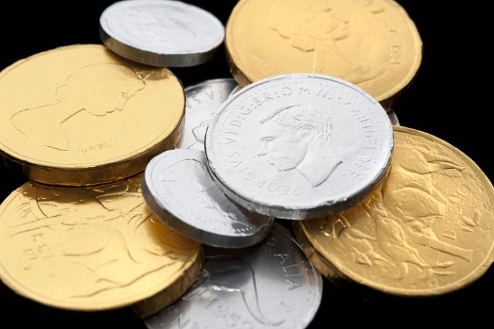 Close-up of chocolate coins wrapped in golden and silver shiny paper on black background