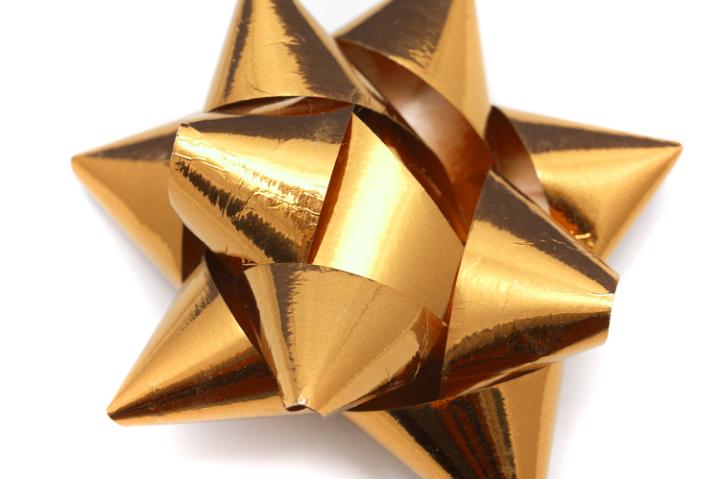 Shiny metallic golden foil ribbon bow for decorating festive gifts in a close up view on white