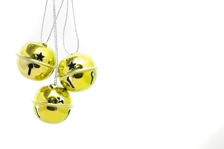 Three hanging gold metal jingle bells commemorating the Christmas song isolated on white with large copyspace