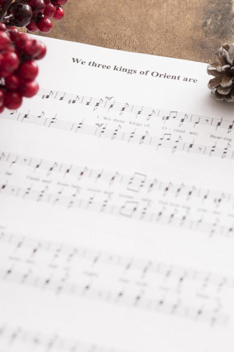 Christmas carol music background with a soft focus view of the score for We Three Kings Of Orient Are with corner decorations of red berries and pine cones