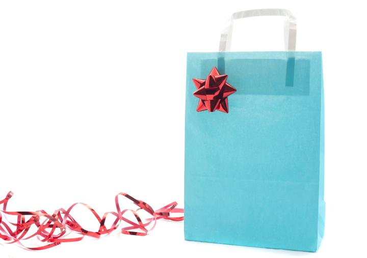 Pale blue paper Christmas gift bag decorated with a red foil bow and ribbon with a blank side for your greeting or copyspace alongside isolated on white