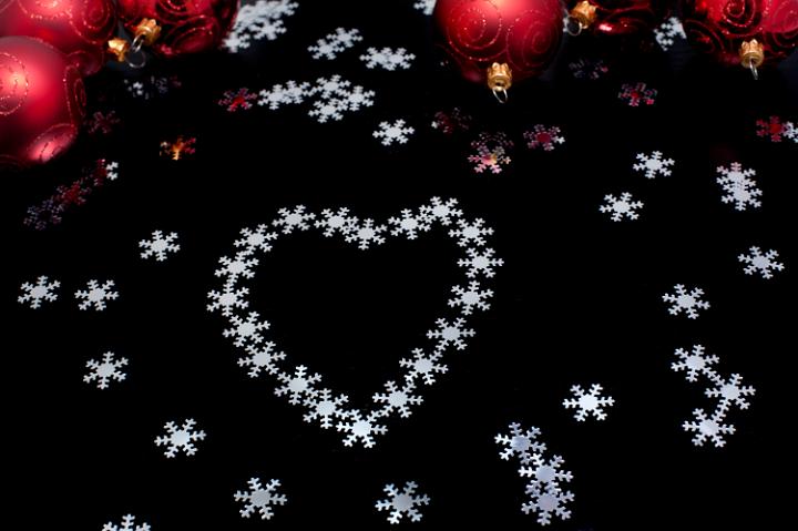 Christmas snowflake heart shape on a black background with scattered snowflakes and colourful Christmas baubles