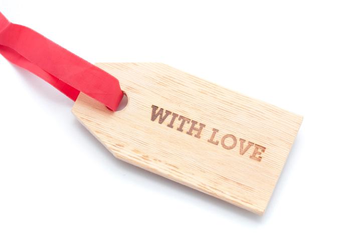 With Love gift tag with a wood grain texture and a festive red ribbon attached over a white background