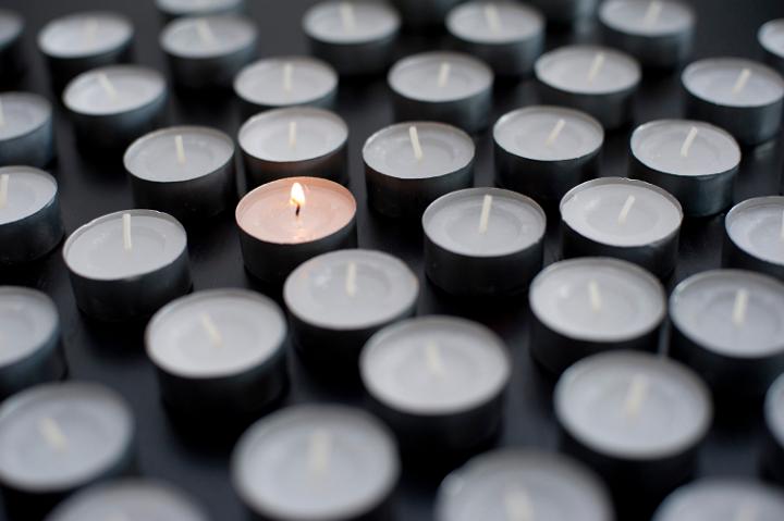 concept image of one lone burning candle in a sea of un-lit lights