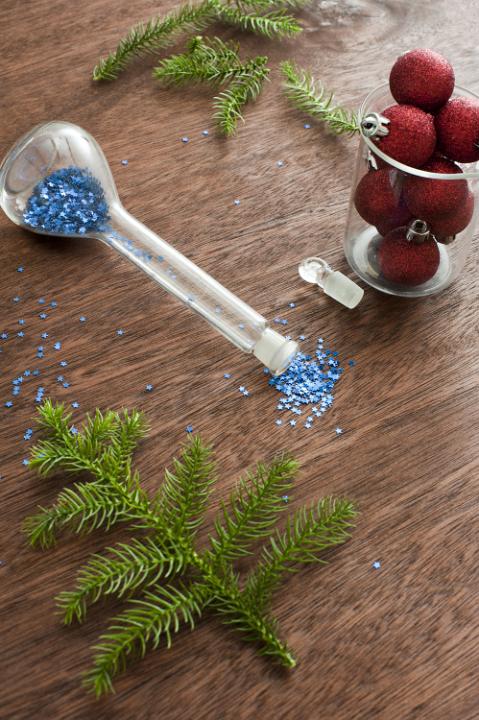 Red Christmas balls, fir tree branch and scattered blue sparkles on wooden table