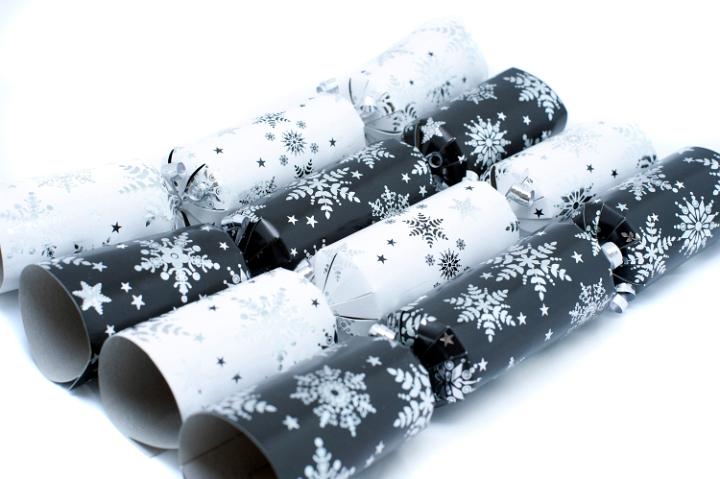 Row of alternating black and white Christmas crackers filled with surprises decorated with snowflakes for a fun table decoration at Christmas dinner
