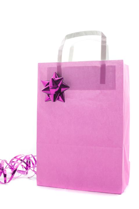 Pink Christmas shopping or gift bag decorated with a metallic bow and twirled ribbon isolated on a white background