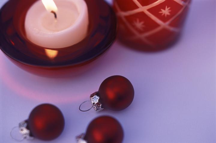 a red coloured festive still life composed of a candles glass holders, christmas balls and