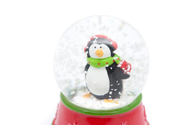 Penguin snow globe to celebrate Christmas with a cute dapper little penguin in a winter scarf and cap standing in swirling snowflakes