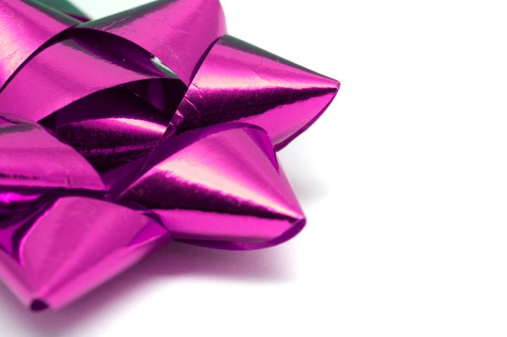 Colourful pink ornamental bow of intricately tied foil ribbon used to decorate gifts and packages over the Christmas season or for a special event, with copyspace