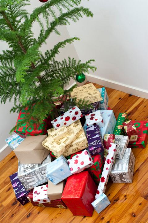 Large collection of colourful gift-wrapped Christmas gifts under a small Xmas tree in preparation for a family celebration of the festive season