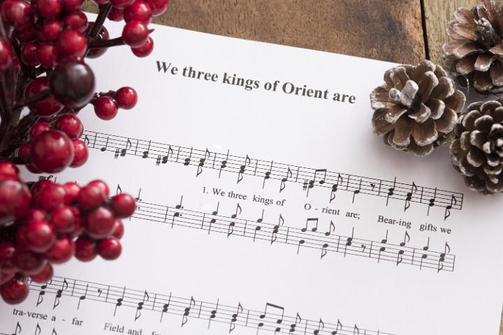 We three kings of Orient are sheet music surrounded by holly berries and frosty open pine cones