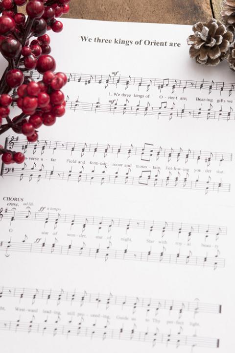 Christmas carol background with a music score decorated with red berries and frosted cones