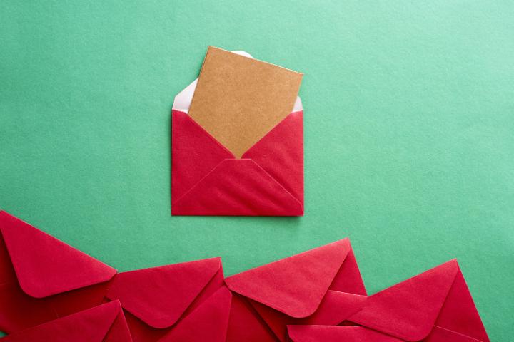 Opened red festive Christmas envelope with a blank brown card protruding from the flap on a green background with a lower border of more red envelopes