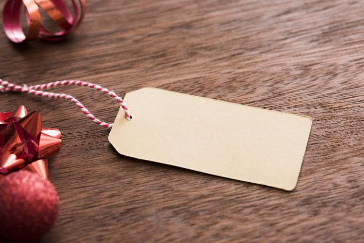 Blank Christmas gift tag with red bow , baubles and ribbon forming a side border over textured wood, copy space for your holiday greeting