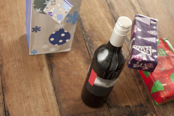 A bottle of wine standing beside some xmas presents on a wooden table