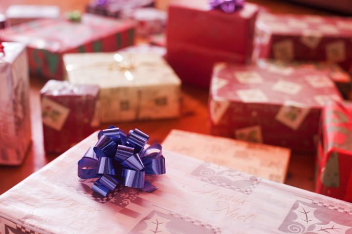 A close up of a purple ribbon on a Christmas present sitting amongst other presents.
