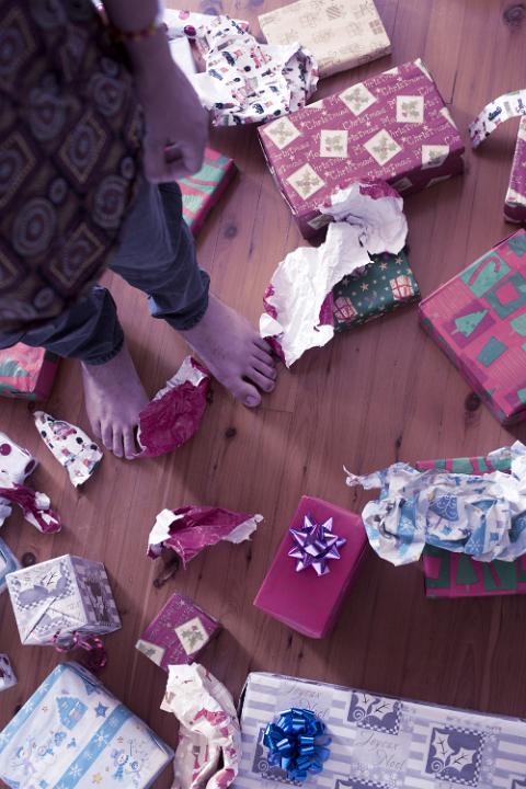 A close up of a child standing amongst unopened Christmas presents and wrapping paper.