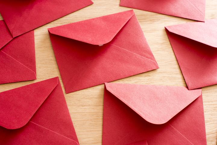 Scattered festive red Christmas envelopes lying face down on a wooden table in a holiday greeting and communications concept