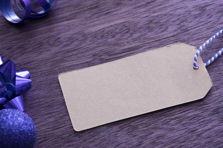 Purple toned blank gift tag lying on wood with a festive border of Christmas baubles and bows with copy space for your greeting