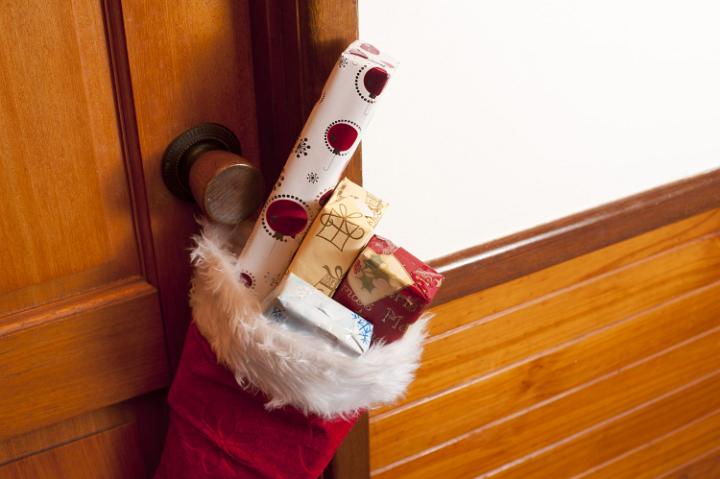 Red Christmas stocking filled with gifts from Santa waiting for a lucky child on Christmas morning hanging on a wooden door handle