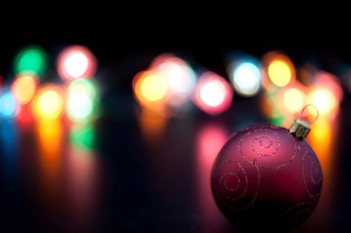 Focus to a single decorative maroon Christmas bauble in the foreground with a colourful Christmas lights bokeh backdrop