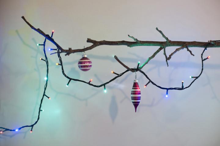 Two Christmas pink balls and lighted garland on leafless branch against of white background.