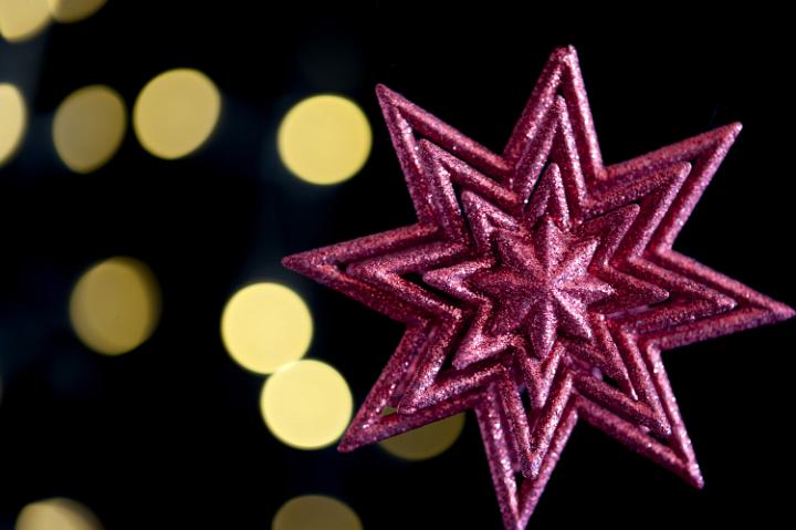 a red coloured glitter star ornament with defuse lights in the background